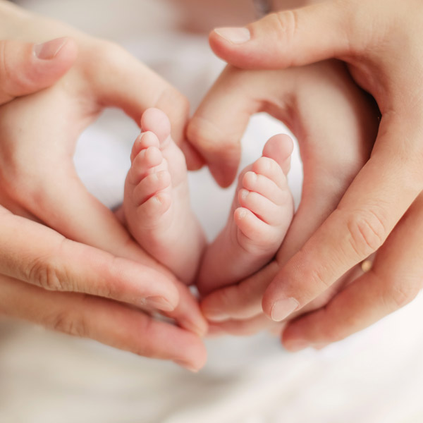 Baby feet with a woman's hands in a heart around the feet, with a man's hands holding the woman's hands.