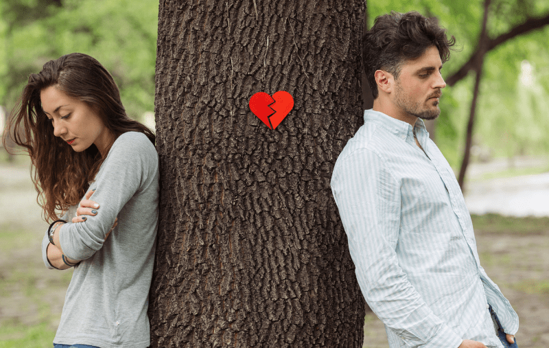 An unhappy couple, facing away from each other with a tree in between them and a broken heart on the tree